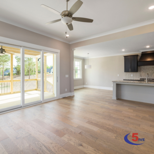 Bright and spacious interior of a modern home featuring wooden flooring, a ceiling fan, and large sliding glass doors leading to an outdoor deck.